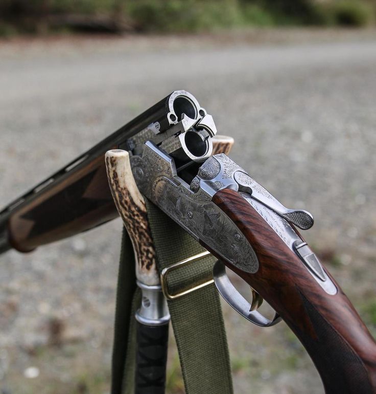 Close-up of two ornate revolvers resting on a wooden-stock hunting rifle with a green sling outdoors.
